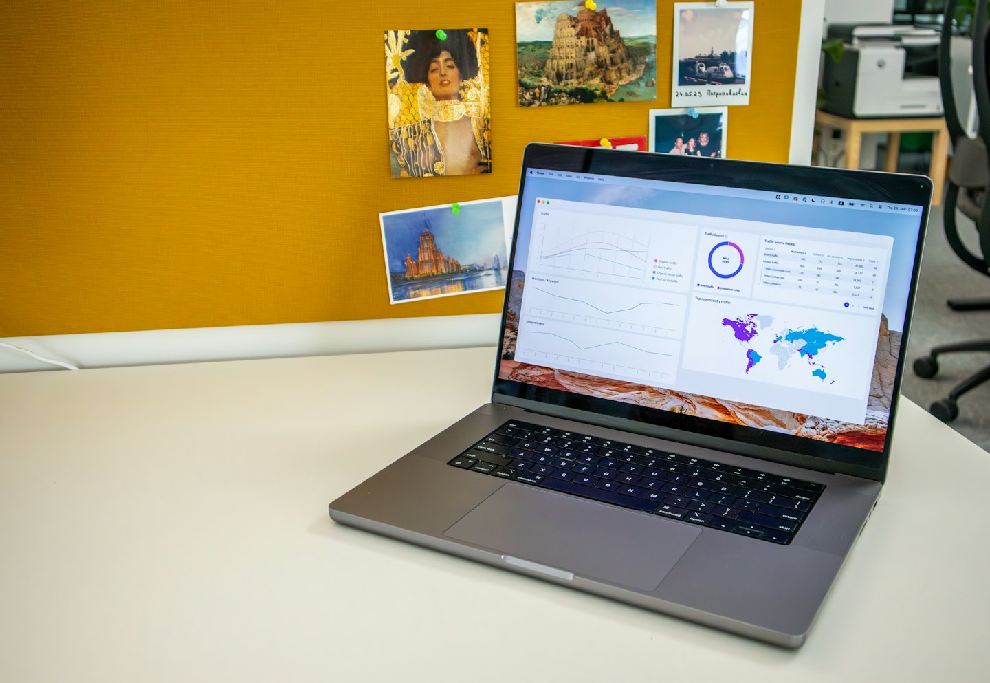 Laptop menampilkan grafik di atas meja putih dengan papan gabus kuning.