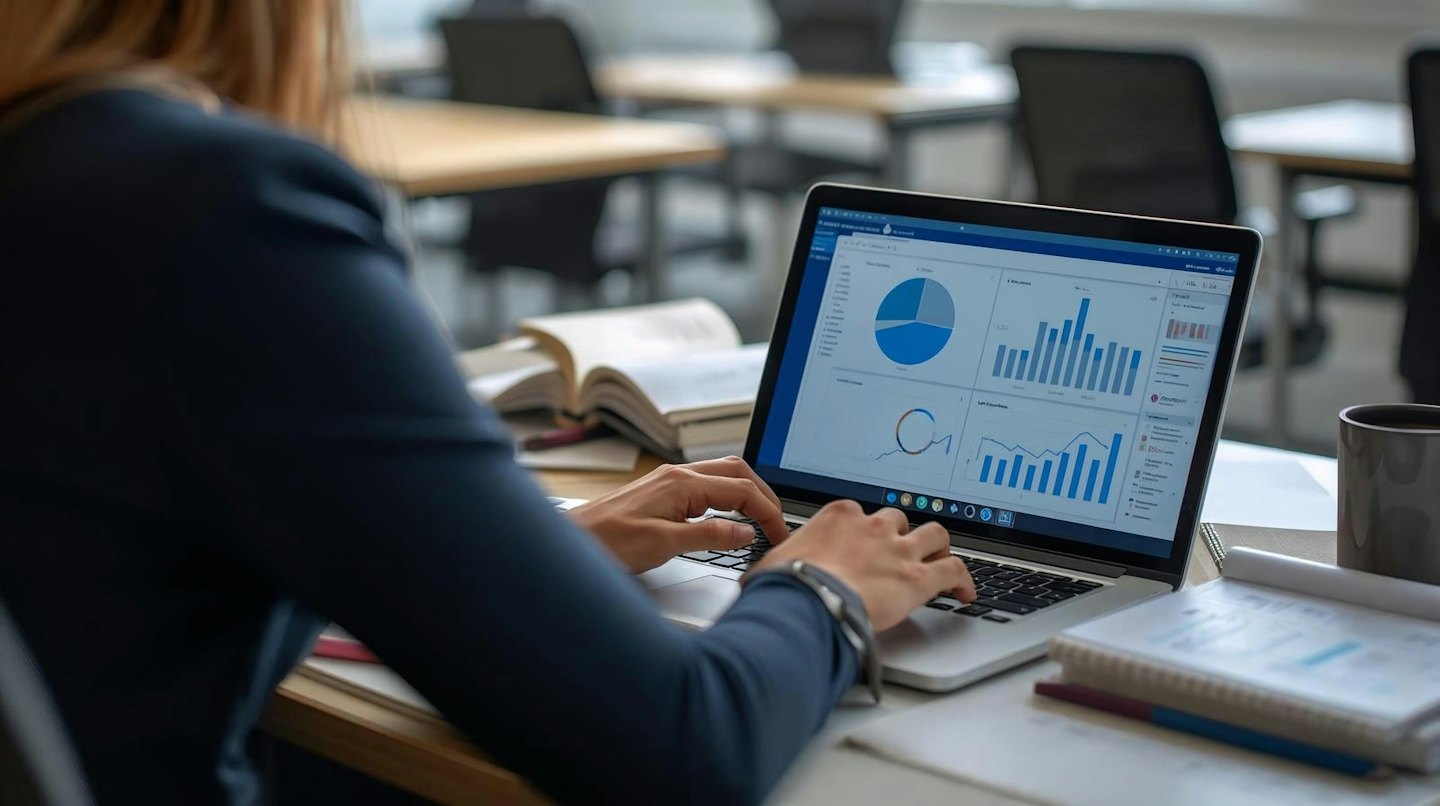 Orang mengetik di laptop dengan grafik bisnis di layar.